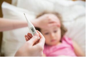 Child in bed running a fever and parent looking at thermometer.